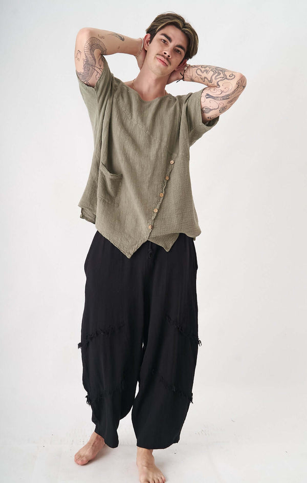 Erkek model, asimetrik düğme detaylı, organik keten-pamuk karışımı üst ve rahat, boho stil pantolon giyiyor.
